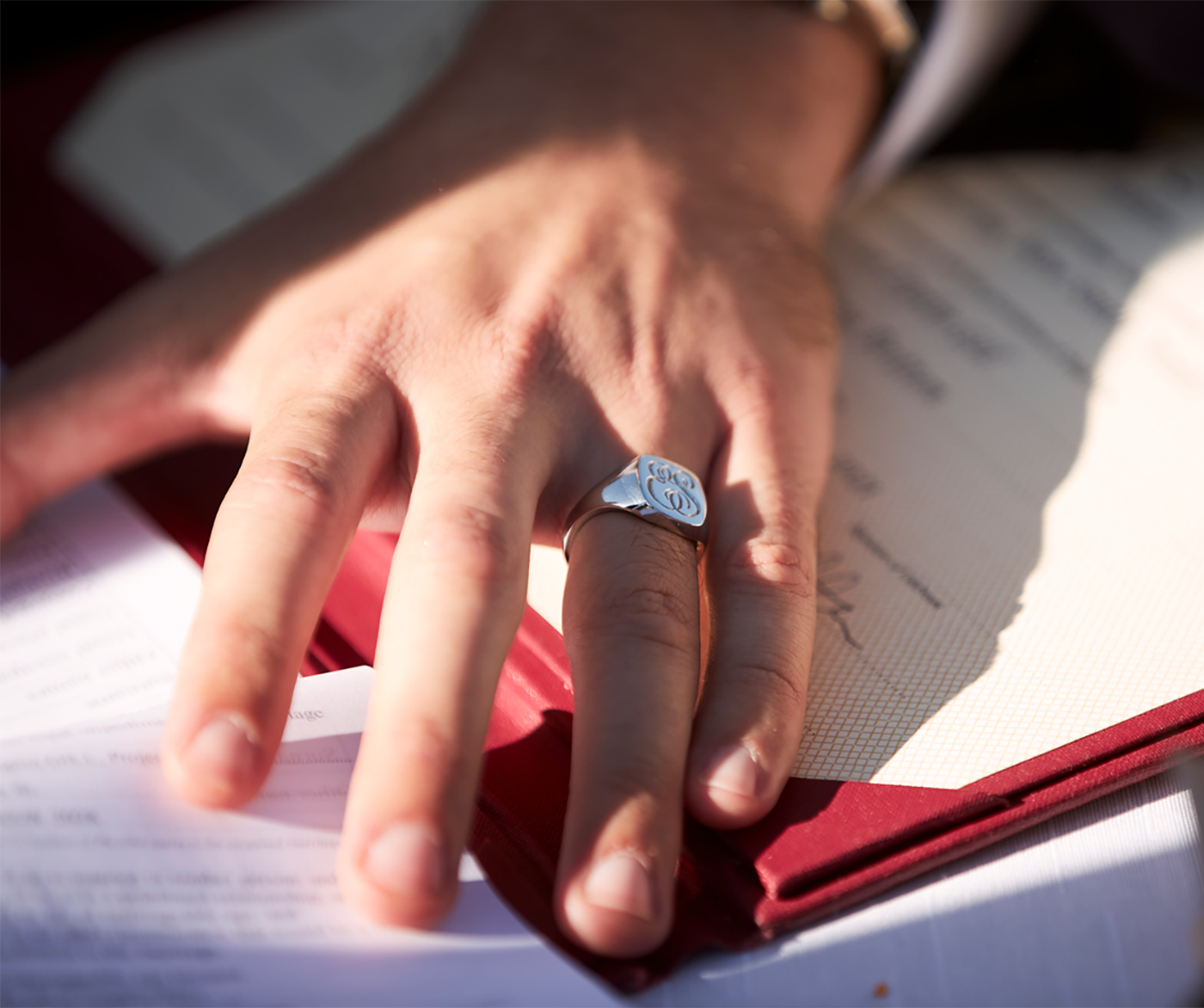 Hand of groom on wedding day wearing bespoke engraved signet ring on his ring finger.